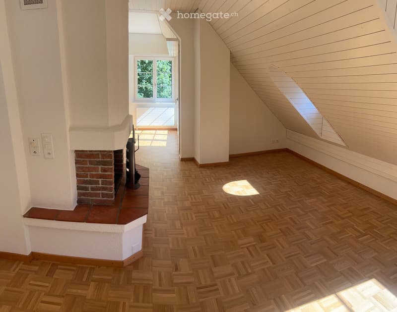 Bright hallway with wooden herringbone flooring, white walls, and a brick fireplace on the left. A window at the end leads to a balcony or outdoor area.