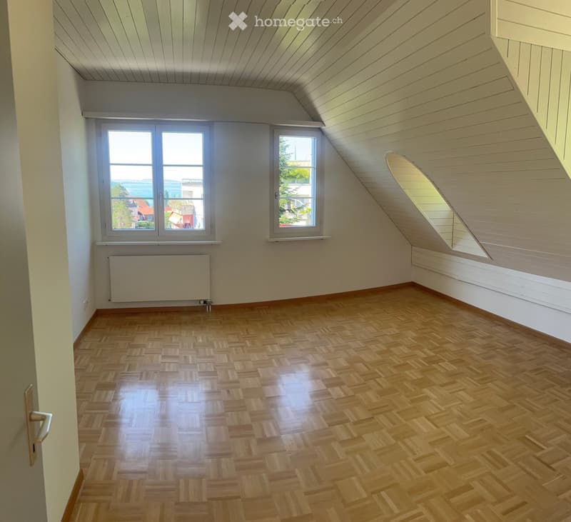 Empty room with wooden herringbone flooring, white walls, and large windows offering a view of the landscape.