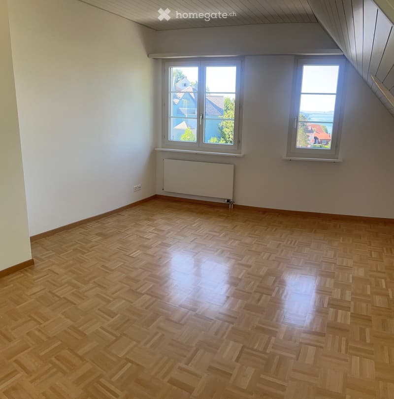 Empty room with wooden herringbone flooring, white walls, and large windows offering a view of the outside. A radiator is mounted on one wall.