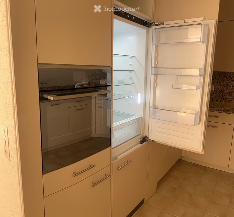 Modern kitchen with light-colored cabinets, an open refrigerator, and an oven. The refrigerator is fully visible with multiple shelves and drawers.