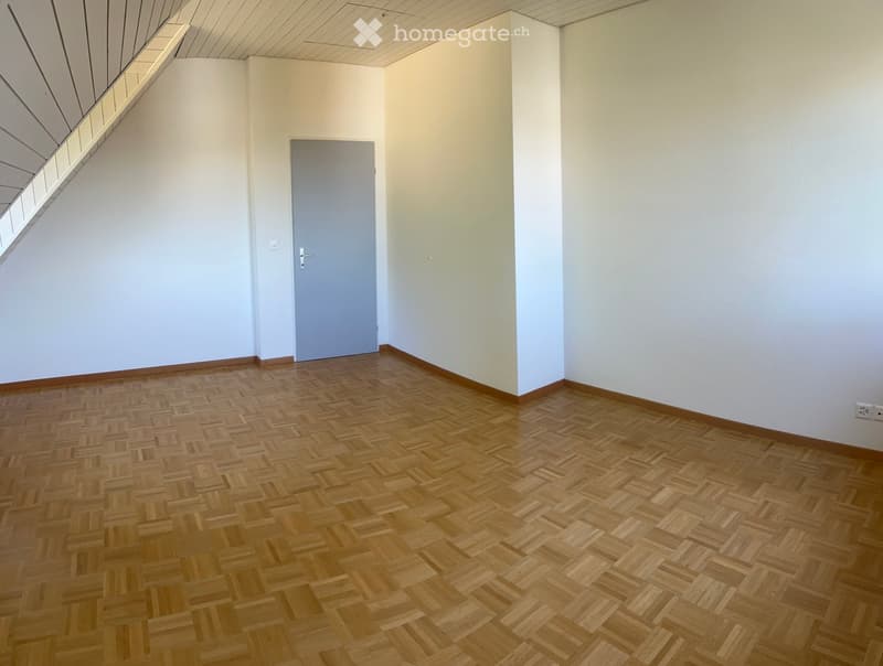 Empty room with wooden herringbone flooring, white walls, and a single door.