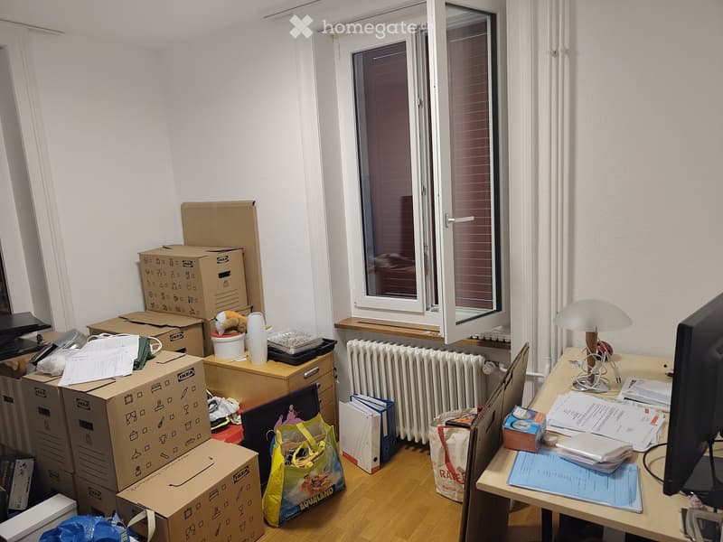 Room with a desk, lamp, screen, radiator, and several cardboard boxes stacked around the space.