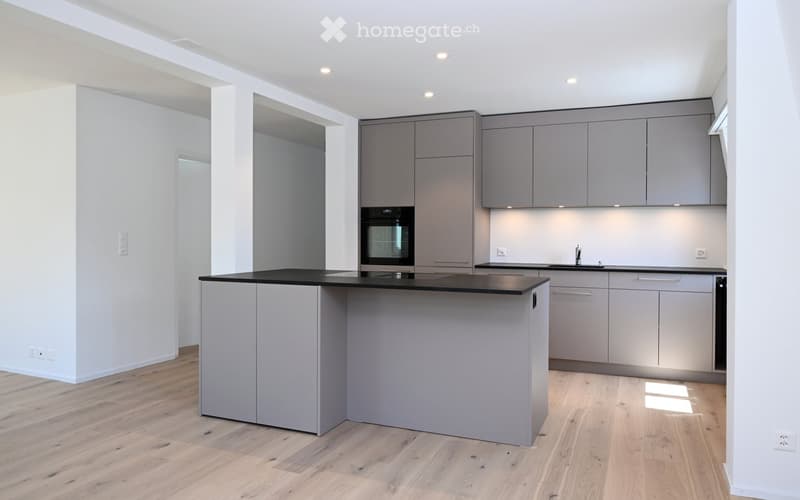 Modern kitchen with grey cabinets, a central island, and a black countertop. Features include a sink with a modern faucet and an integrated oven.