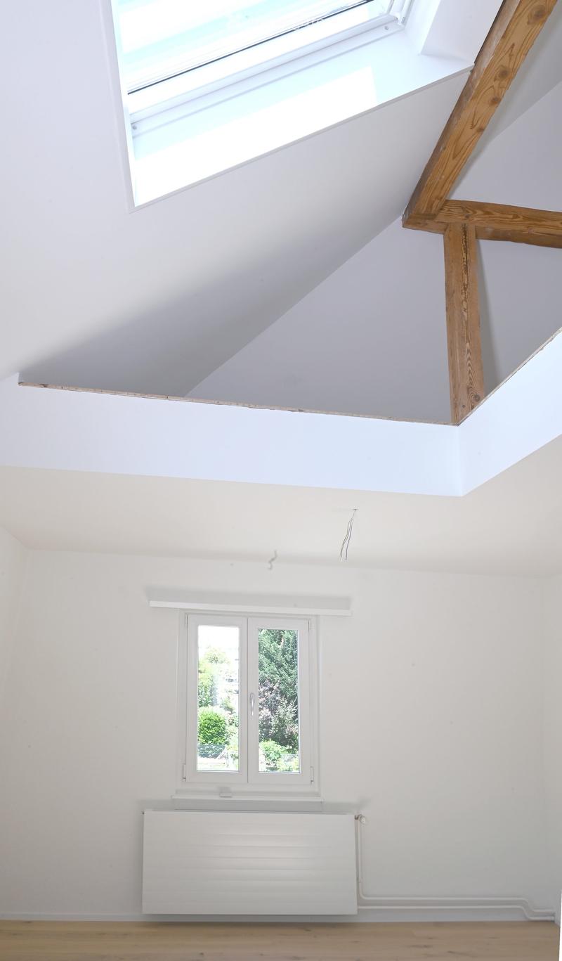 Bright, empty attic room with wooden floor, white walls, skylight window, and a radiator. No furniture or equipment present.