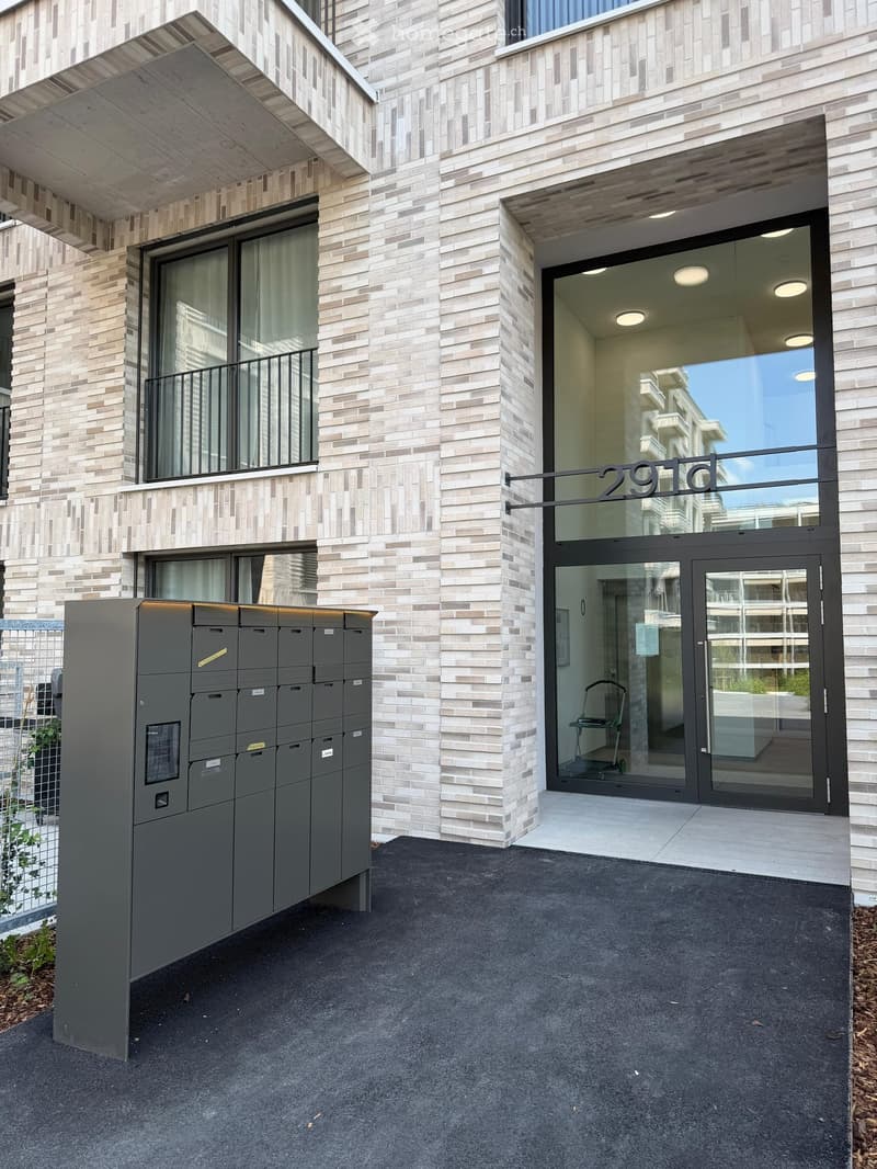 Modern building entrance with glass doors, mailboxes, and a balcony visible above.