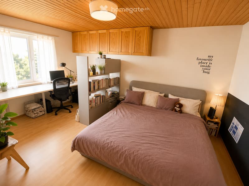 Cozy bedroom with a large bed, desk area, bookshelf, and decorative plants. Features wooden flooring, built-in cabinets, and a motivational quote on the wall.
