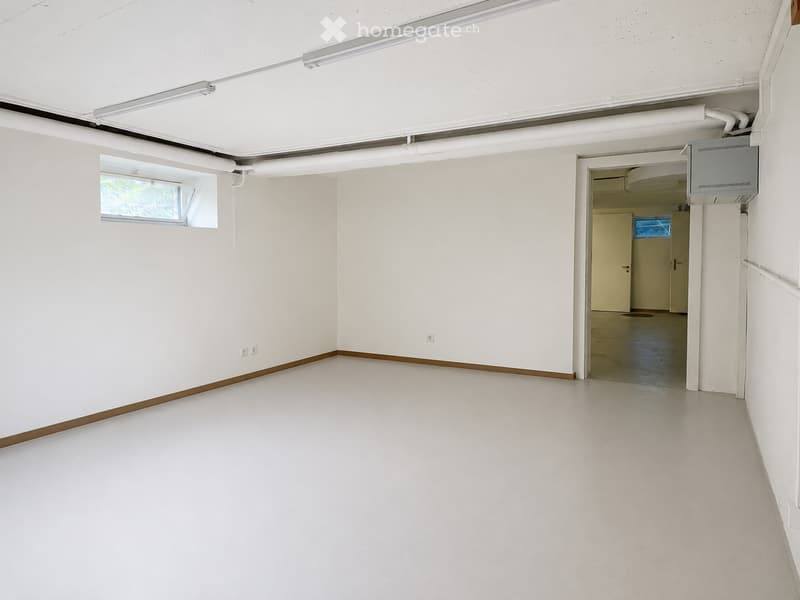 Empty room with white walls, a white floor, and a small window on one wall. There is a doorway leading to another room.
