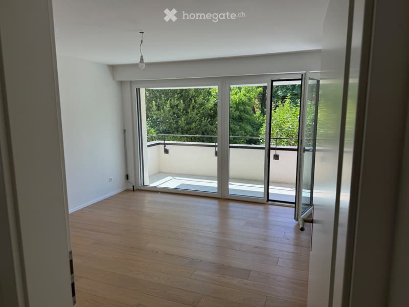 Empty room with wooden flooring, white walls, and large sliding glass doors leading to a balcony with a metal railing and outdoor space.