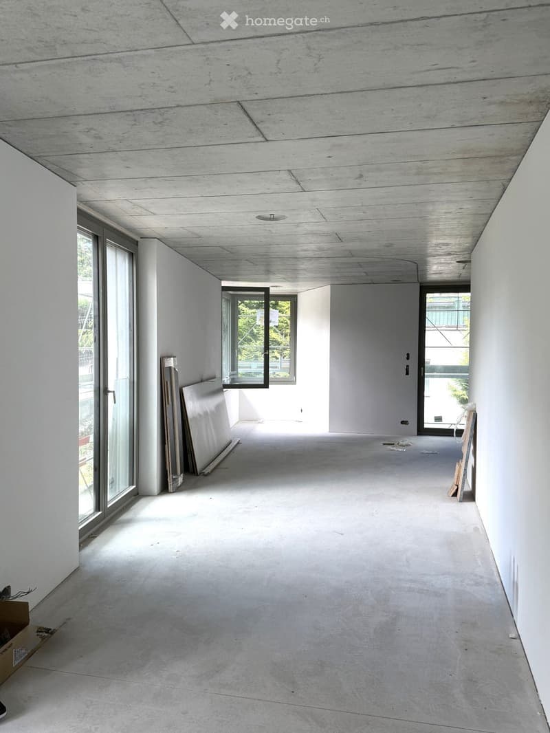 Empty room with white walls, concrete floor, and large windows. No furniture or equipment present.