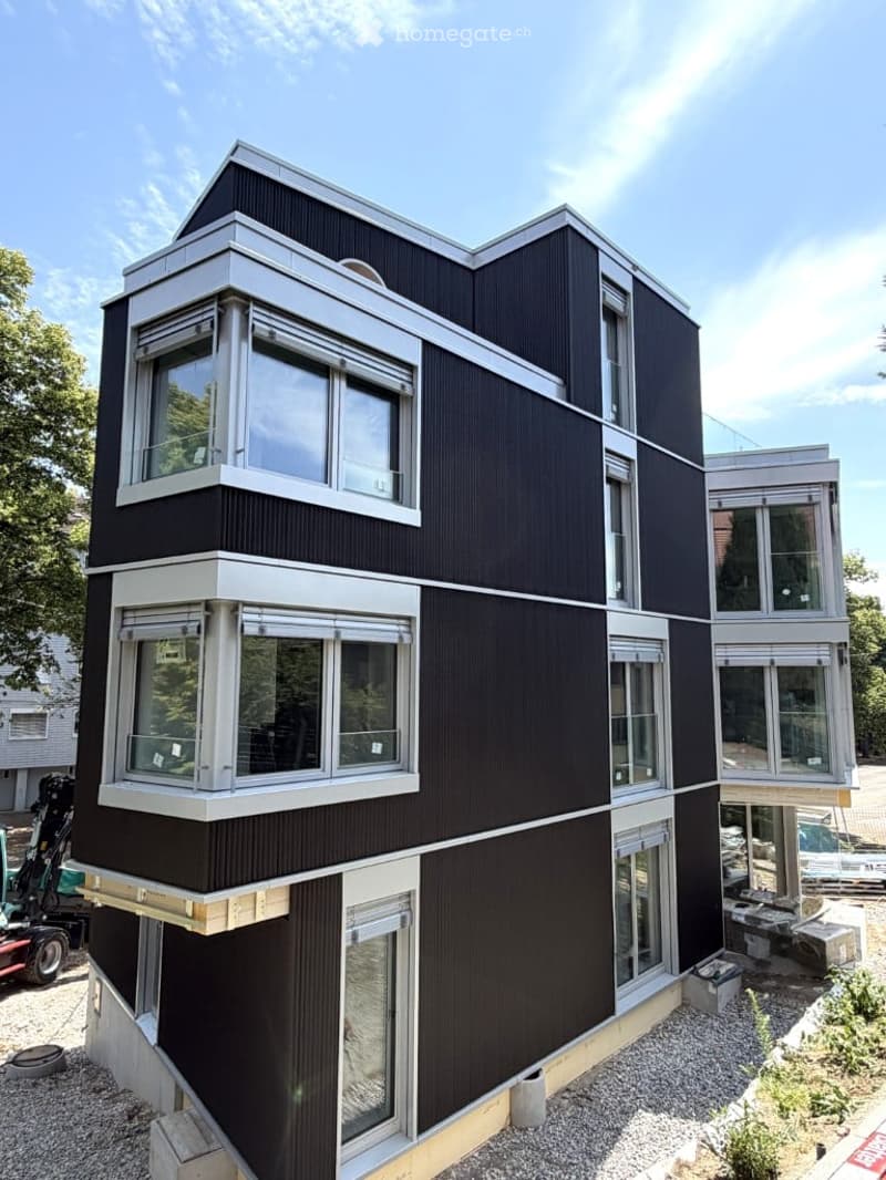 Modern two-story building with black and white exterior, large windows, raised ground floor, and construction materials visible around the base.