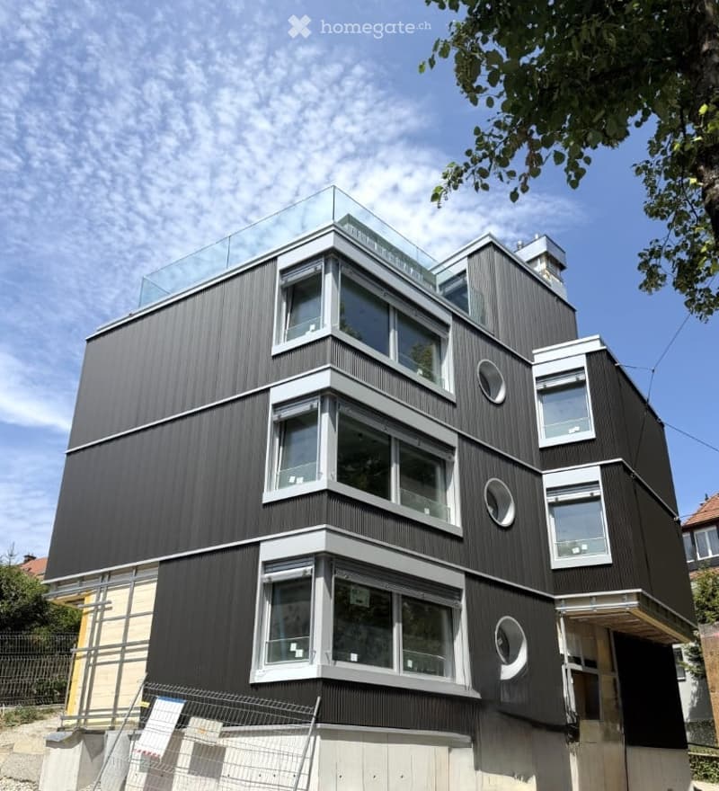 Modern, multi-story building with dark wood siding, large windows, and a glass rooftop terrace.