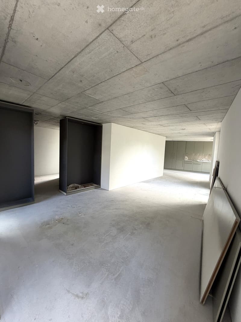 Empty room with concrete floors and walls, exposed ceiling beams, and a small closet area. No furniture or equipment is present.