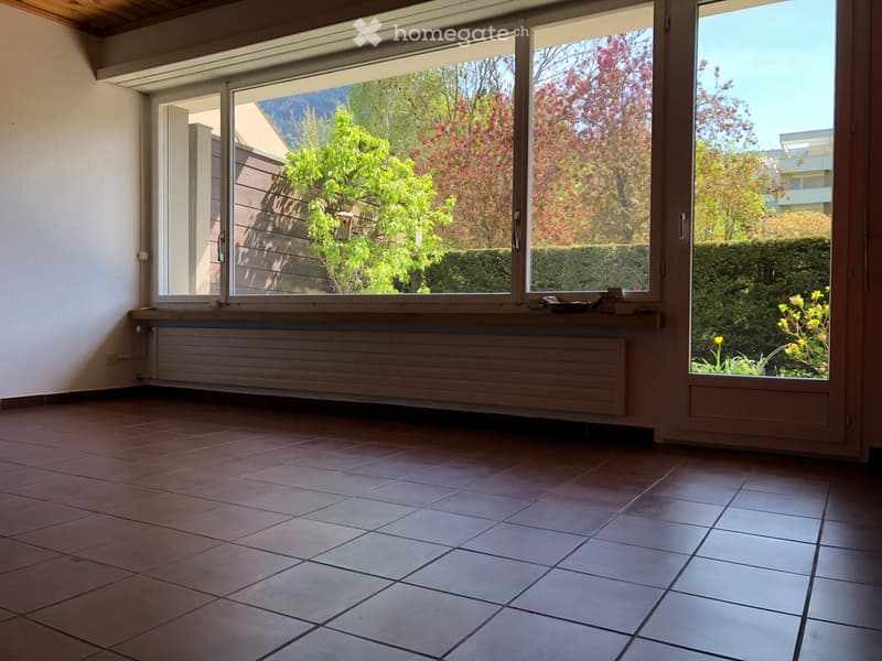 Empty room with tiled floor, large windows, radiator, and view of greenery outside.