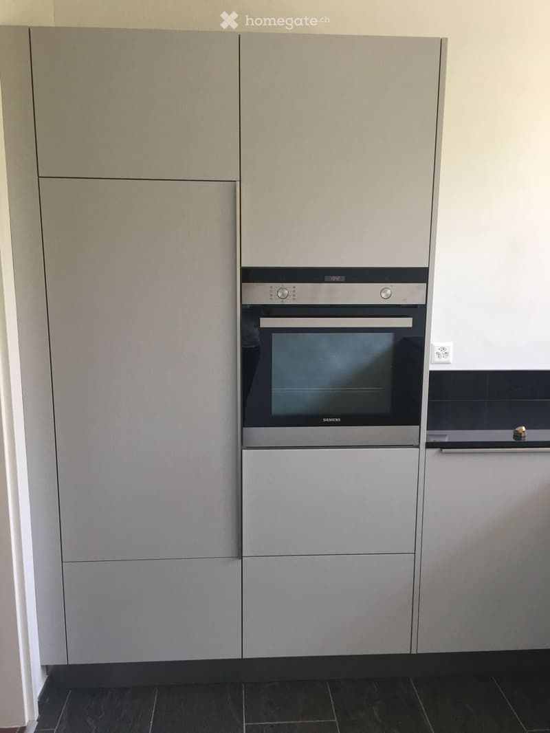 Modern kitchen with grey cabinets and a built-in Siemens oven, dark tiled floor.
