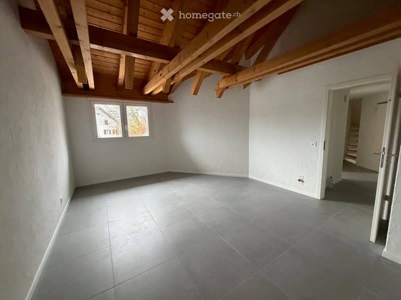 Empty room, exposed wooden beams, tiled floor, two windows, entrance with a staircase.