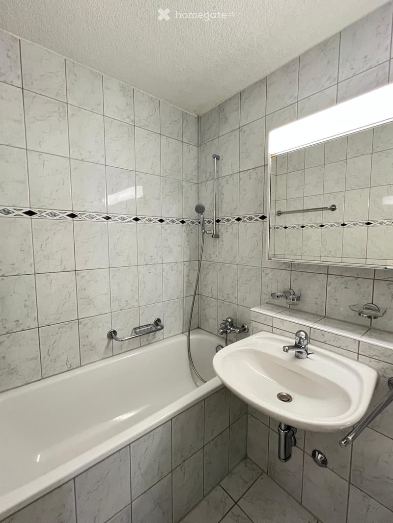 Bathroom with a white bathtub, a sink with a chrome faucet, a mirror, a showerhead, and handrails for accessibility.