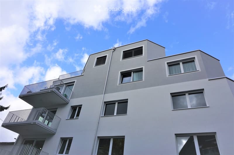 Modern multi-story building with grey facade, multiple windows, and balconies on each level.