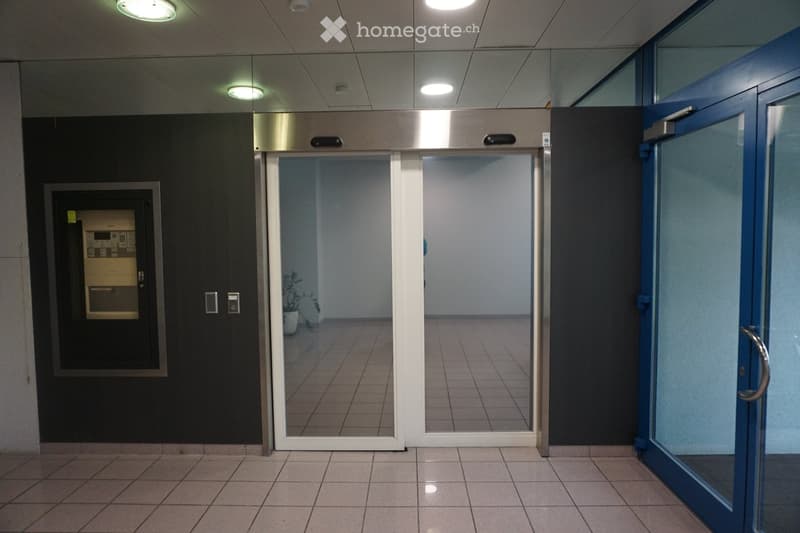 Modern hallway with tiled flooring, recessed ceiling lights, elevator doors, and a control panel on the left wall.