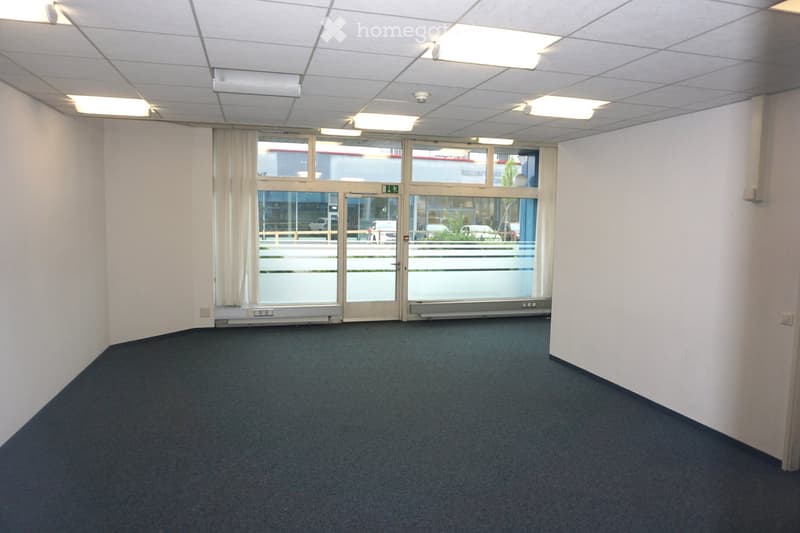 Empty room with white walls, carpeted floor, large glass doors with curtains, and ceiling lights.