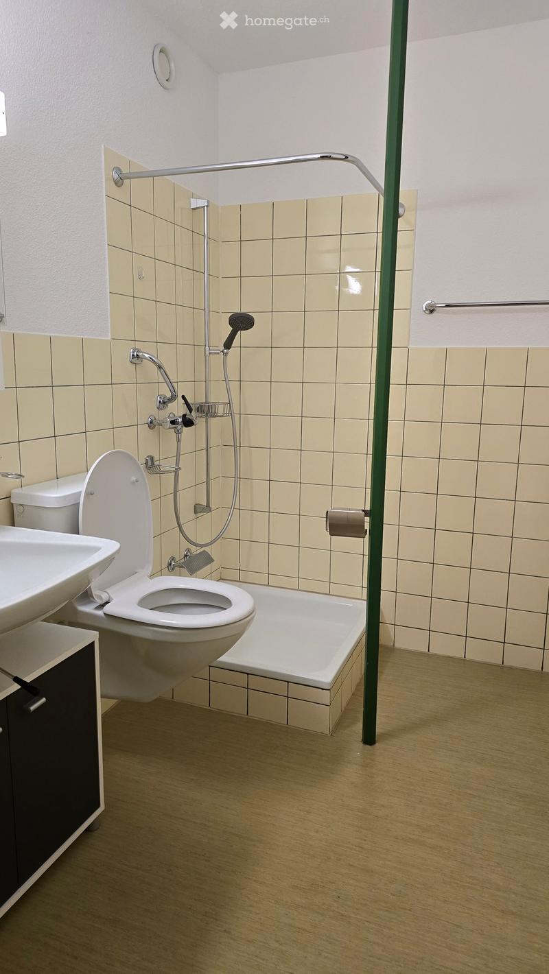 Modern bathroom with beige tiled walls, a bathtub, toilet, sink, and a glass-enclosed shower area.