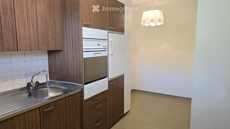 Modern kitchen with wooden cabinets, stainless steel sink, built-in oven, refrigerator, and a hanging light fixture.