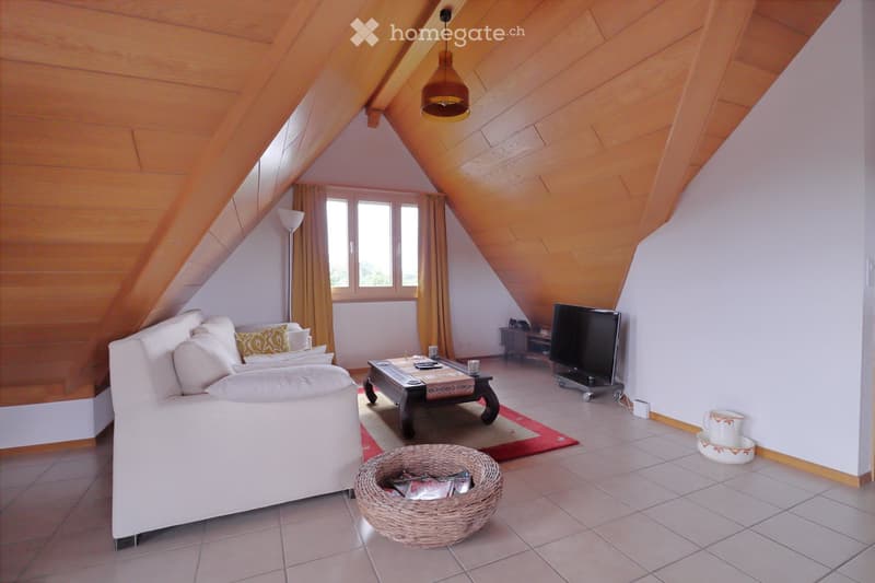 Bright living room with slanted wooden ceiling, white sofa, coffee table, wicker basket, TV, and large windows with curtains.