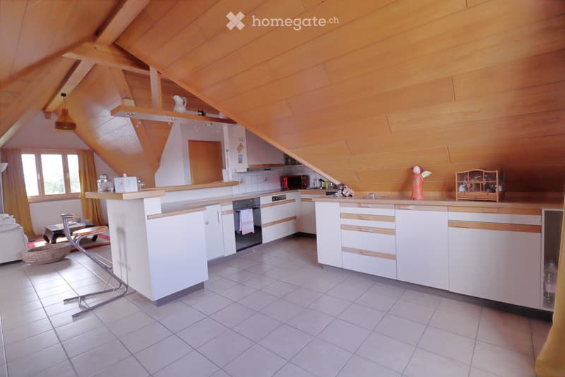 Bright kitchen with white cabinets, wooden accents, and a central island. Features include an oven, microwave, stools, a small table, and decorative items like a vase and birdcage.