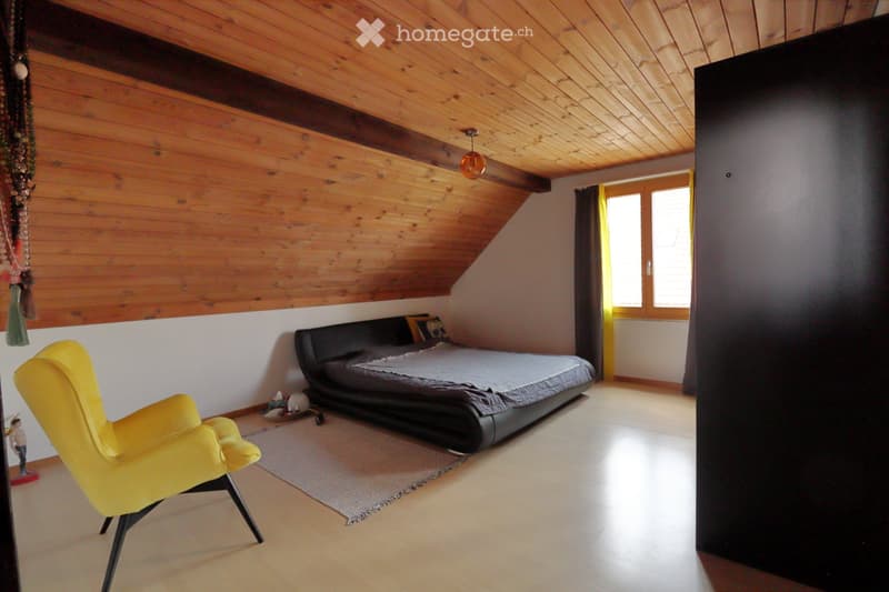 Modern bedroom with wooden slanted ceiling, large window, black leather bed, yellow armchair, and a small rug.
