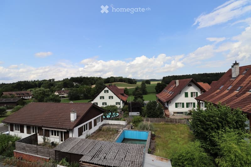Aerial view of a residential area with multiple houses, red-tiled roofs, and a swimming pool in the foreground.