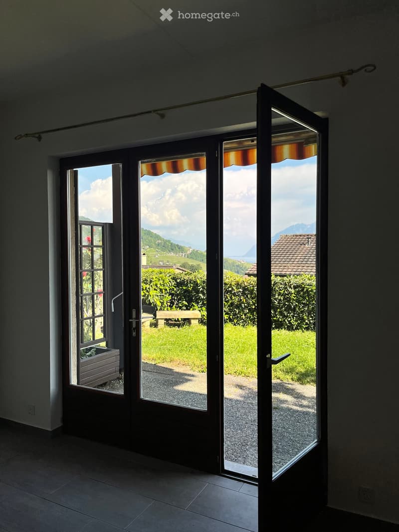 Open doorway leading to a scenic outdoor area with a grassy lawn, a bench, and distant mountains.