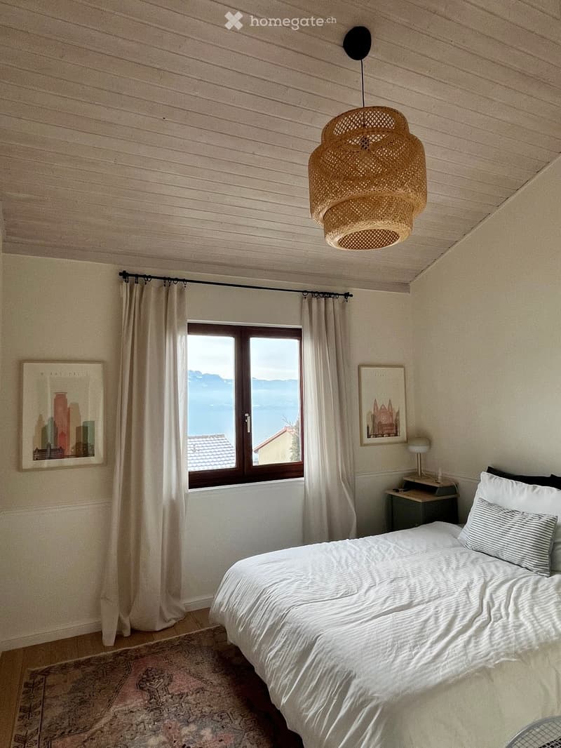 Cozy bedroom with a large bed, nightstand, table lamp, and scenic view through a window with curtains.
