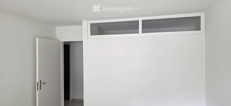 Empty room with white walls, a door, and a small window above the doorway.