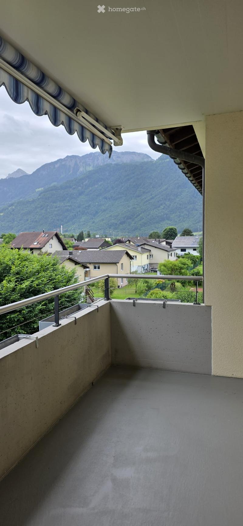 Balcony with metal railing, overlooking a scenic mountain view and surrounding houses.