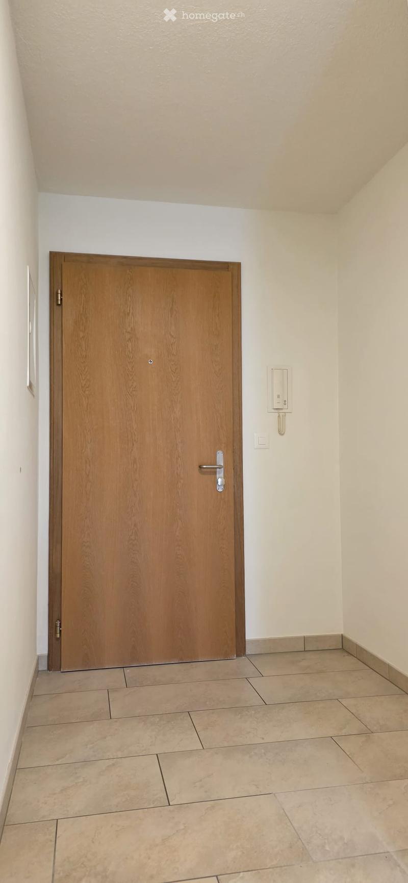 Empty hallway with tiled floor, wooden door, and intercom system on the wall.