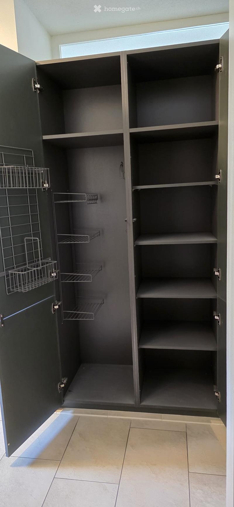 Empty pantry with dark grey cabinets, wire baskets, and tiled floor.