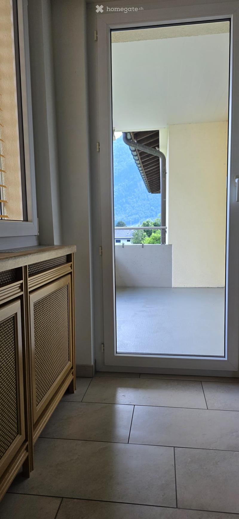 Hallway with tiled floor, radiator on left, sliding glass door leading to balcony with metal railing and scenic view.