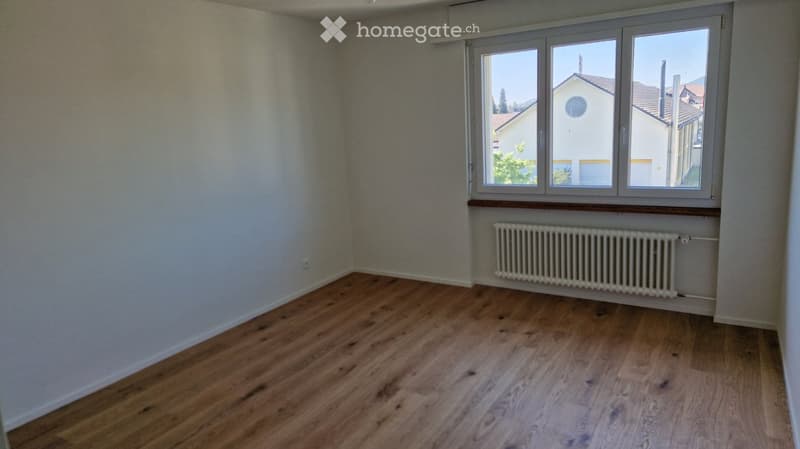Empty room with wooden flooring, white walls, and a window with a radiator below it.