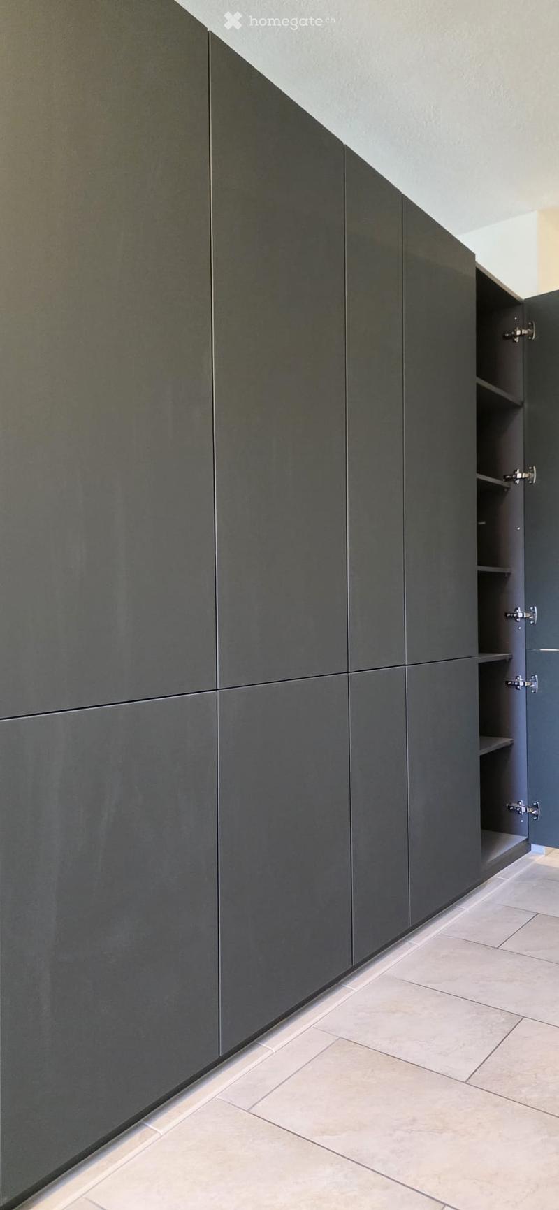 Modern, minimalist hallway with grey built-in cabinets and light-colored tiled flooring.