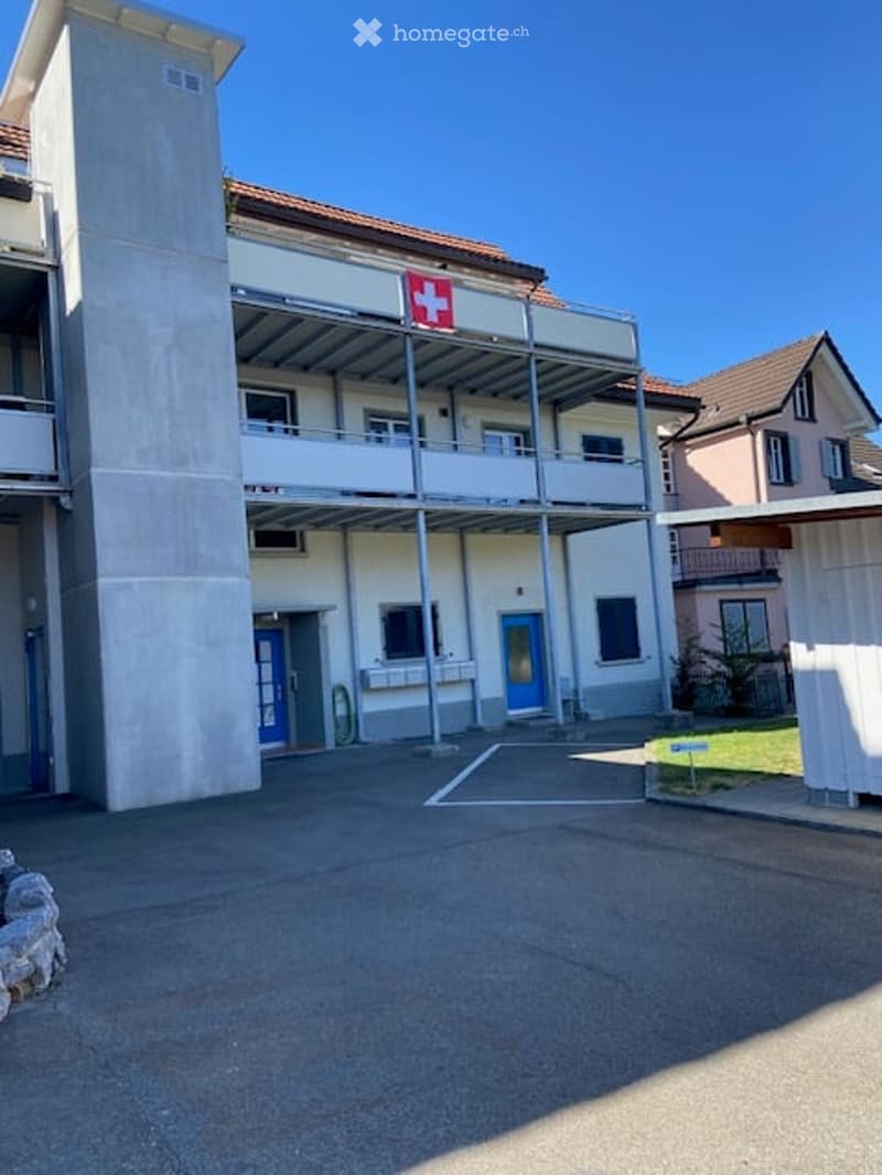 A modern multi-story building with a Swiss flag, featuring balconies, blue doors, and a concrete facade.