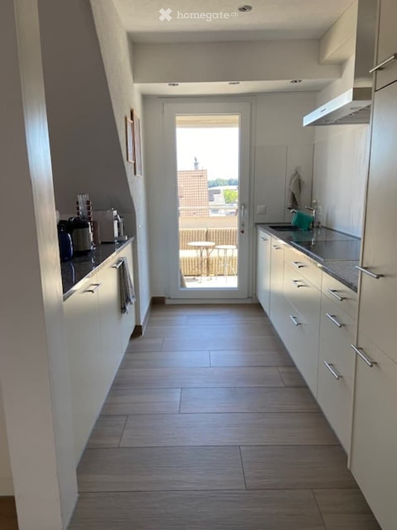 Modern kitchen with white cabinets, stainless steel sink, coffee maker, and a sliding door leading to a balcony.