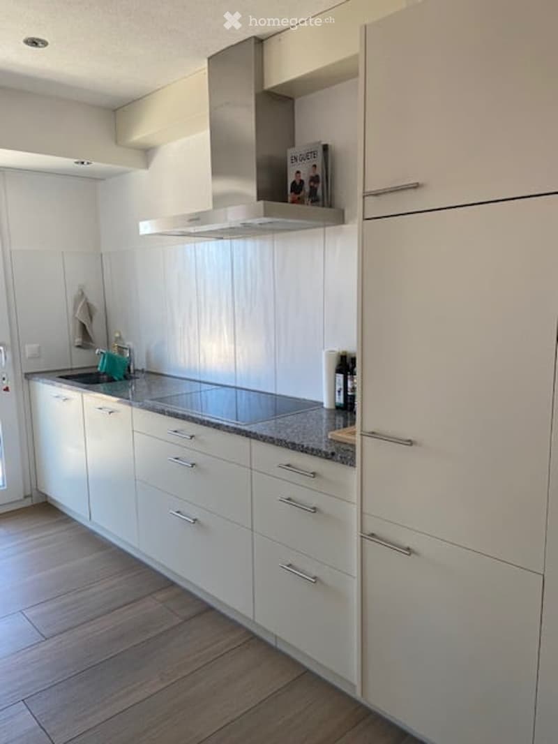 Modern kitchen with white cabinets, granite countertop, stainless steel range hood, and a sink with a faucet. A few decorative items, including books and a bottle, are placed on the countertop.