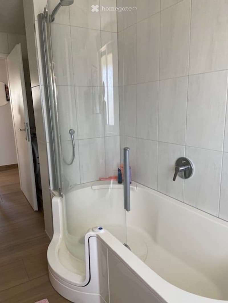 Modern bathroom with a white bathtub, glass-enclosed shower stall, and a chrome faucet.