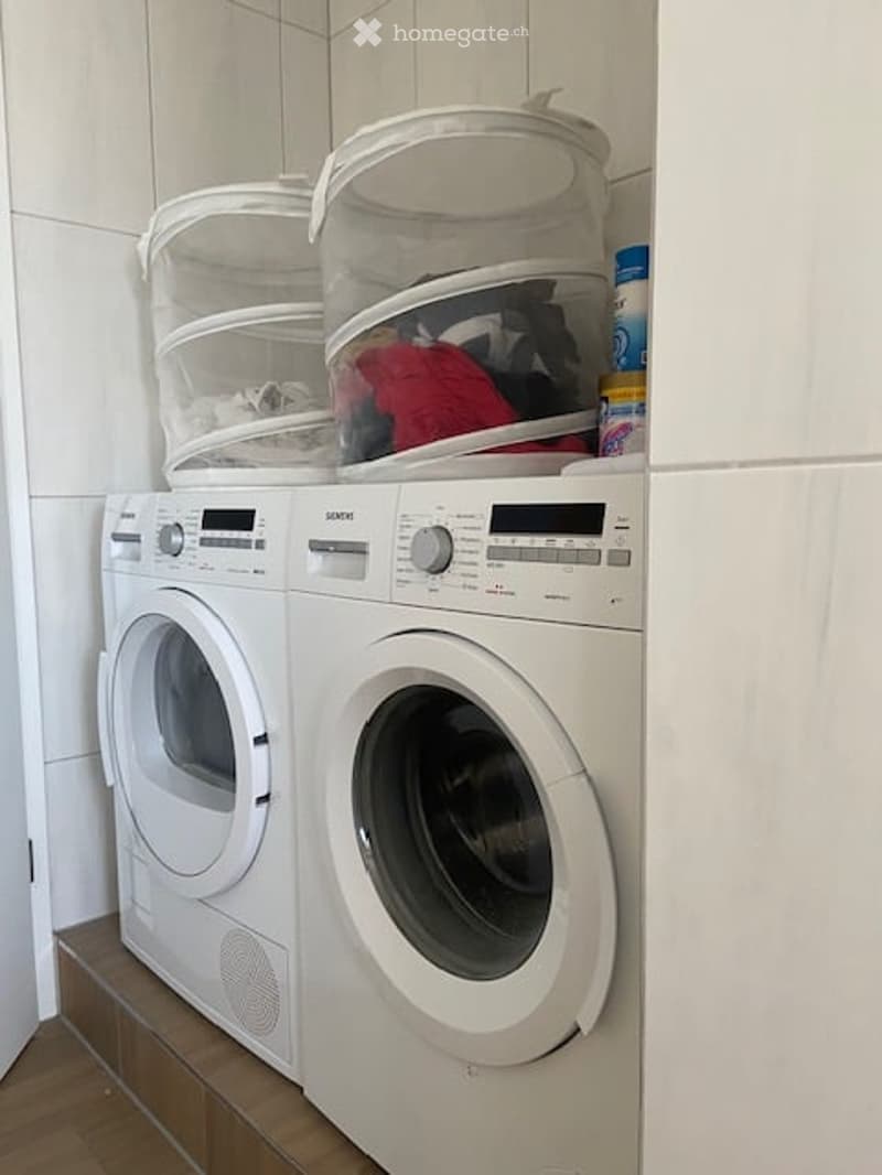 Compact bathroom with a white washing machine and dryer stacked side by side, topped with laundry baskets.