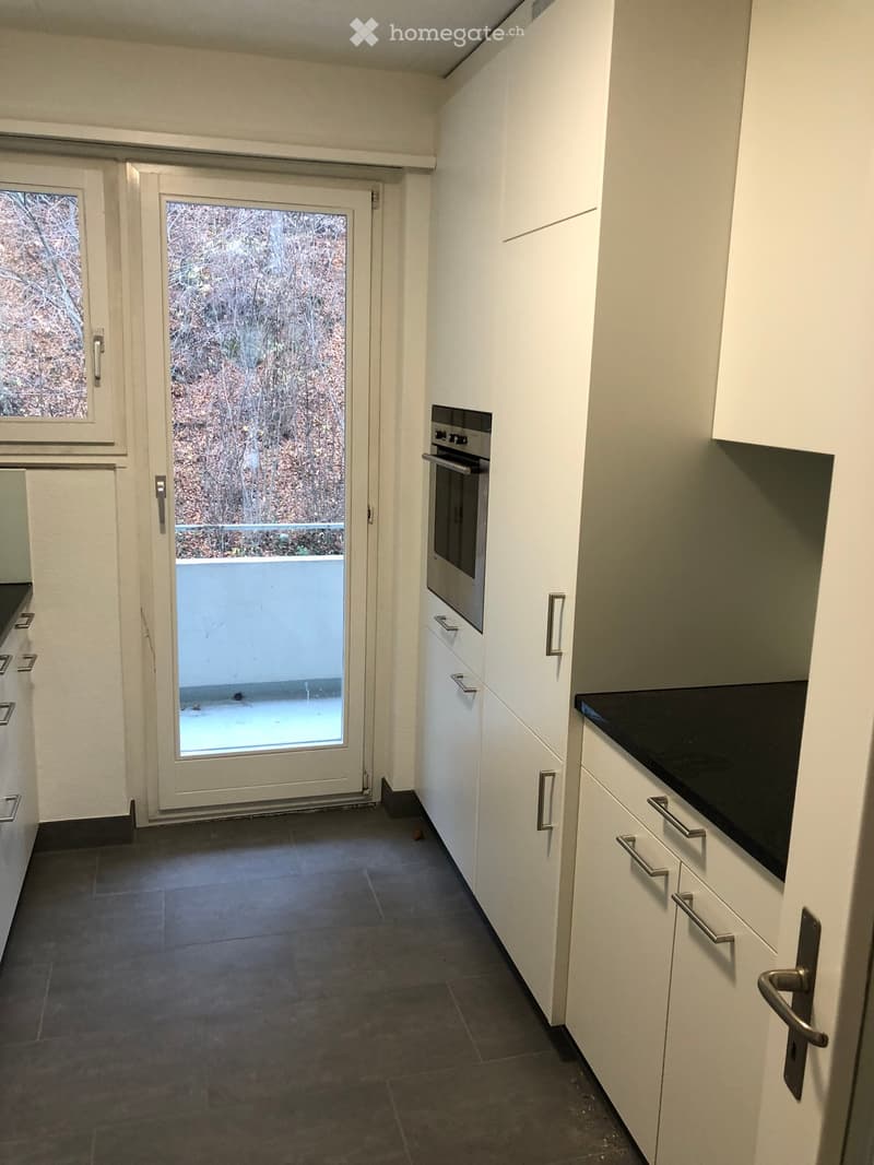 Modern kitchen with white cabinets, dark countertops, and a built-in oven. The space features a large sliding door leading to an outdoor area.
