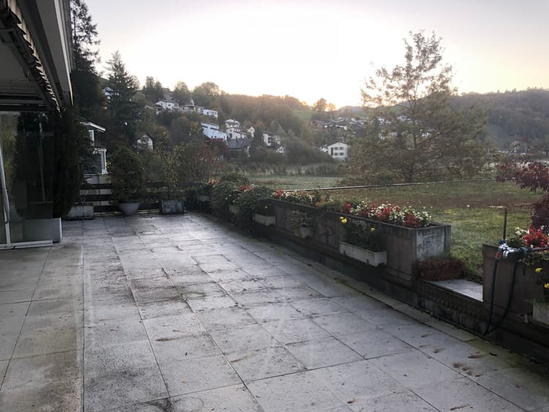 Balcony with tiled floor, low concrete planters with flowers, and a view of a town and surrounding landscape.