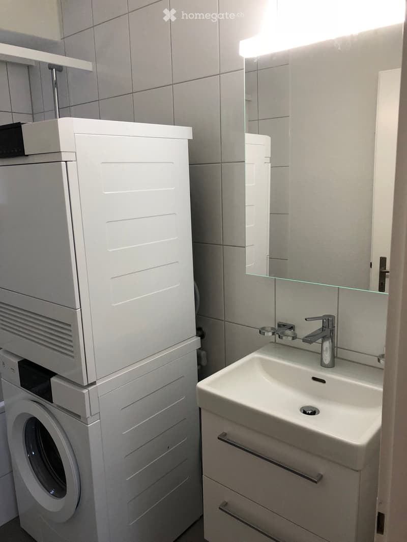 Modern bathroom with a white sink, chrome faucet, mirror, and a stacked washing machine and dryer unit.