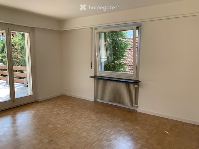 Empty room with wooden flooring, large window, radiator, and sliding glass door leading to a balcony.