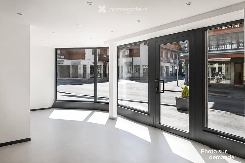 Empty room with large glass doors leading to a street view, white walls, and a grey floor.