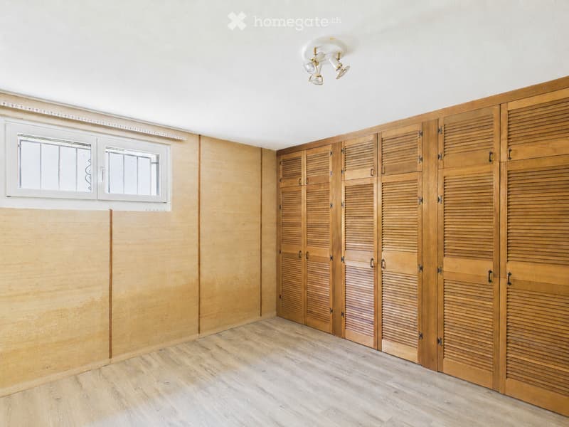Empty room with wooden walls, wooden floor, and built-in wooden closet units. Two windows with white frames are visible on one wall.