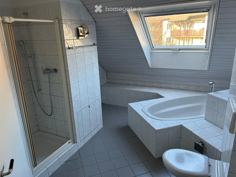 Modern bathroom with a bathtub, toilet, and walk-in shower. Features tiled walls and floor, a large window, and built-in seating next to the bathtub.